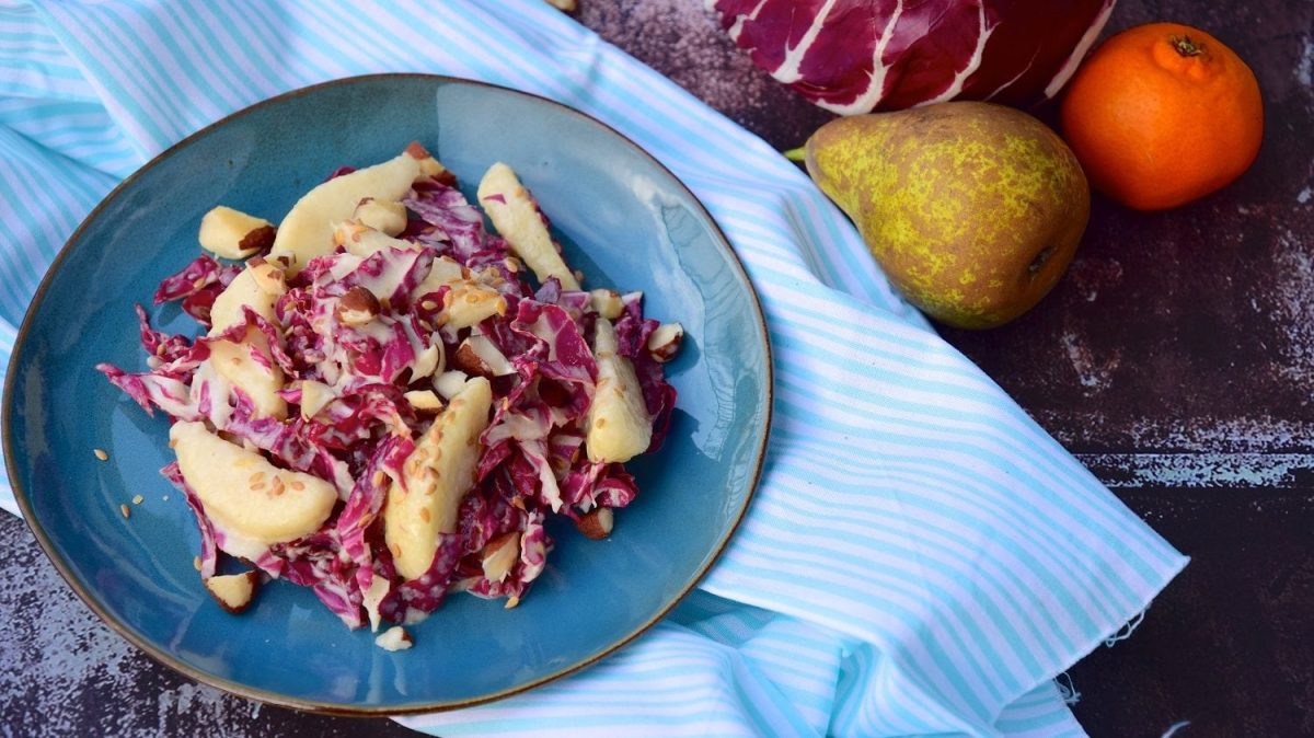 Draufsicht: ein Teller Radicchio-Salat mit Birnen und Paranüssen. Daneben liegen ein Raddichio, eine Birne und eine Orange.