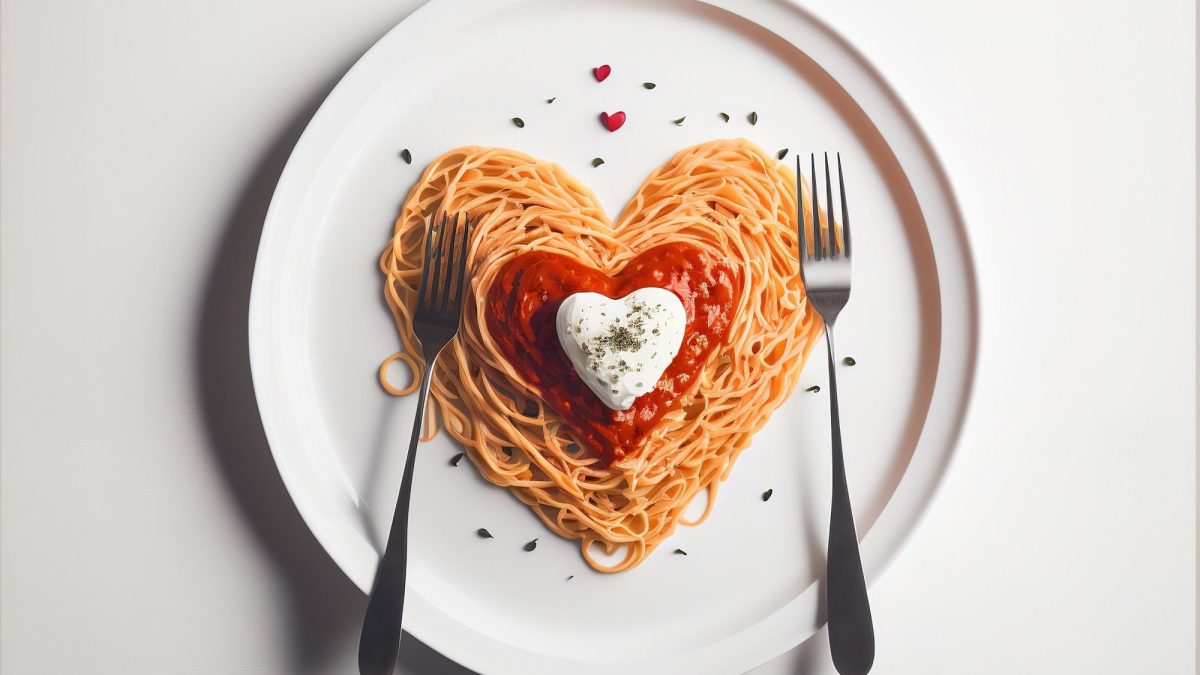 Ein Teller Spaghetti mit Marinara-Sauce, alles in Herzform drapiert, dazu zwei Gabeln, Draufsicht.