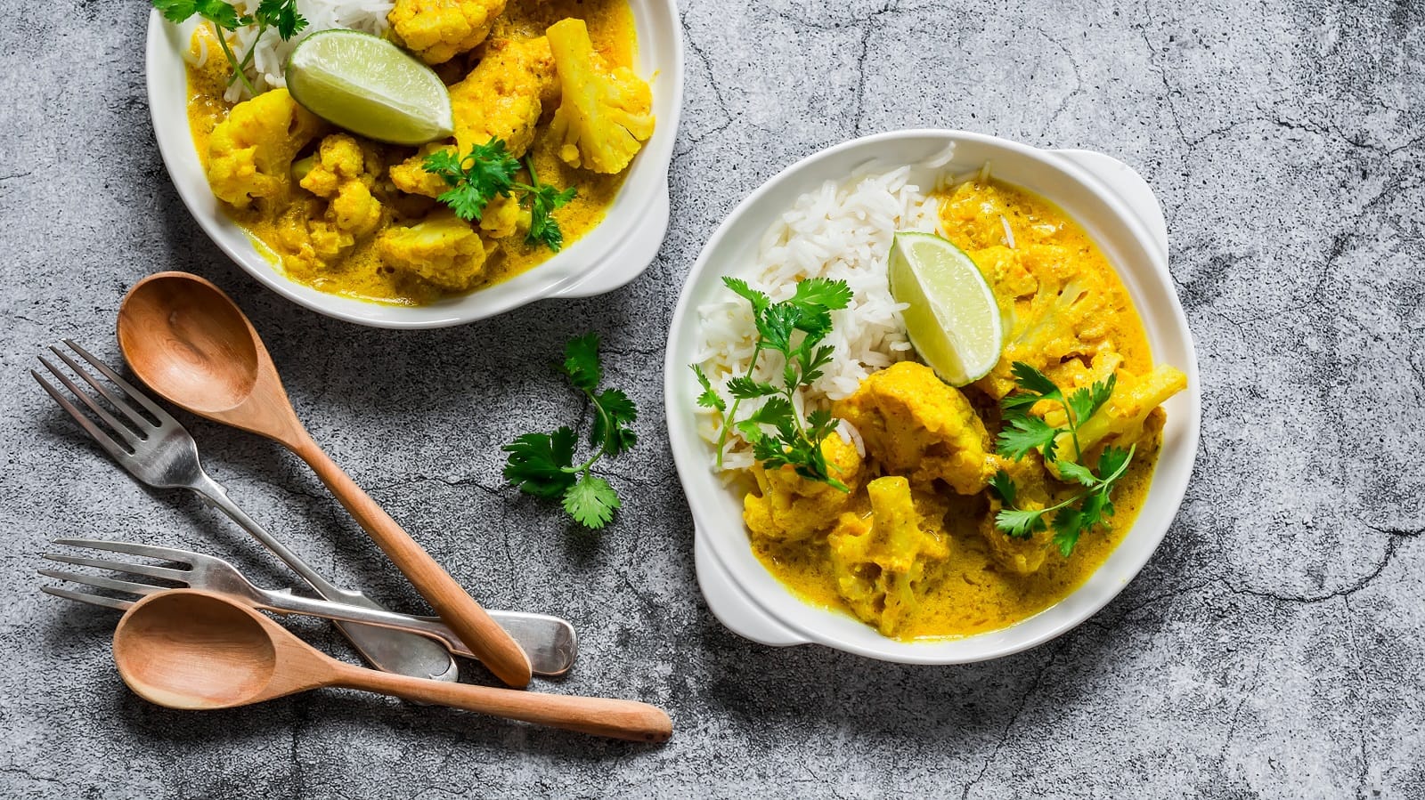 Zwei tiefe Teller mit Bananen-Curry mit Blumenkohl auf einem grauen Tisch.