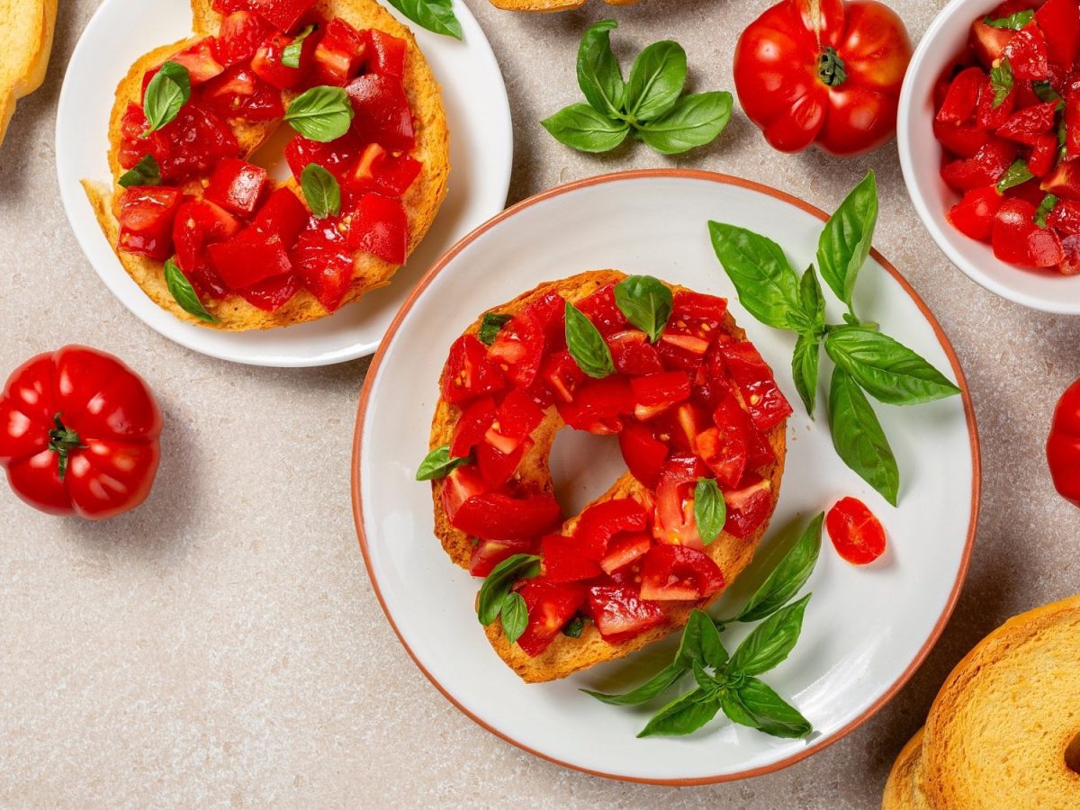 Draufsicht: Italienische Friselle mit frischen Tomaten und Basilikum liegen auf einem hellen Untergrund.