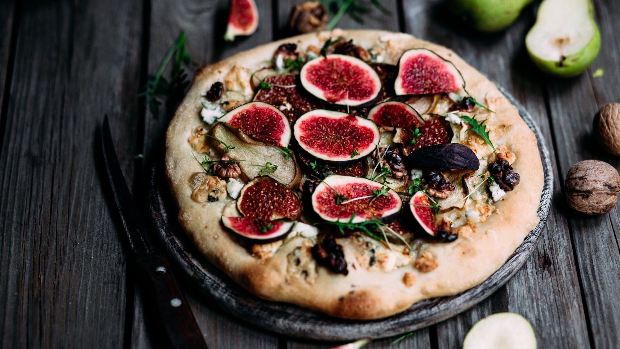 Draufsicht: Gorgonzola-Pizza mit Feigen und Birnen und Nüssen liegt auf einem dunklen Untergrund.