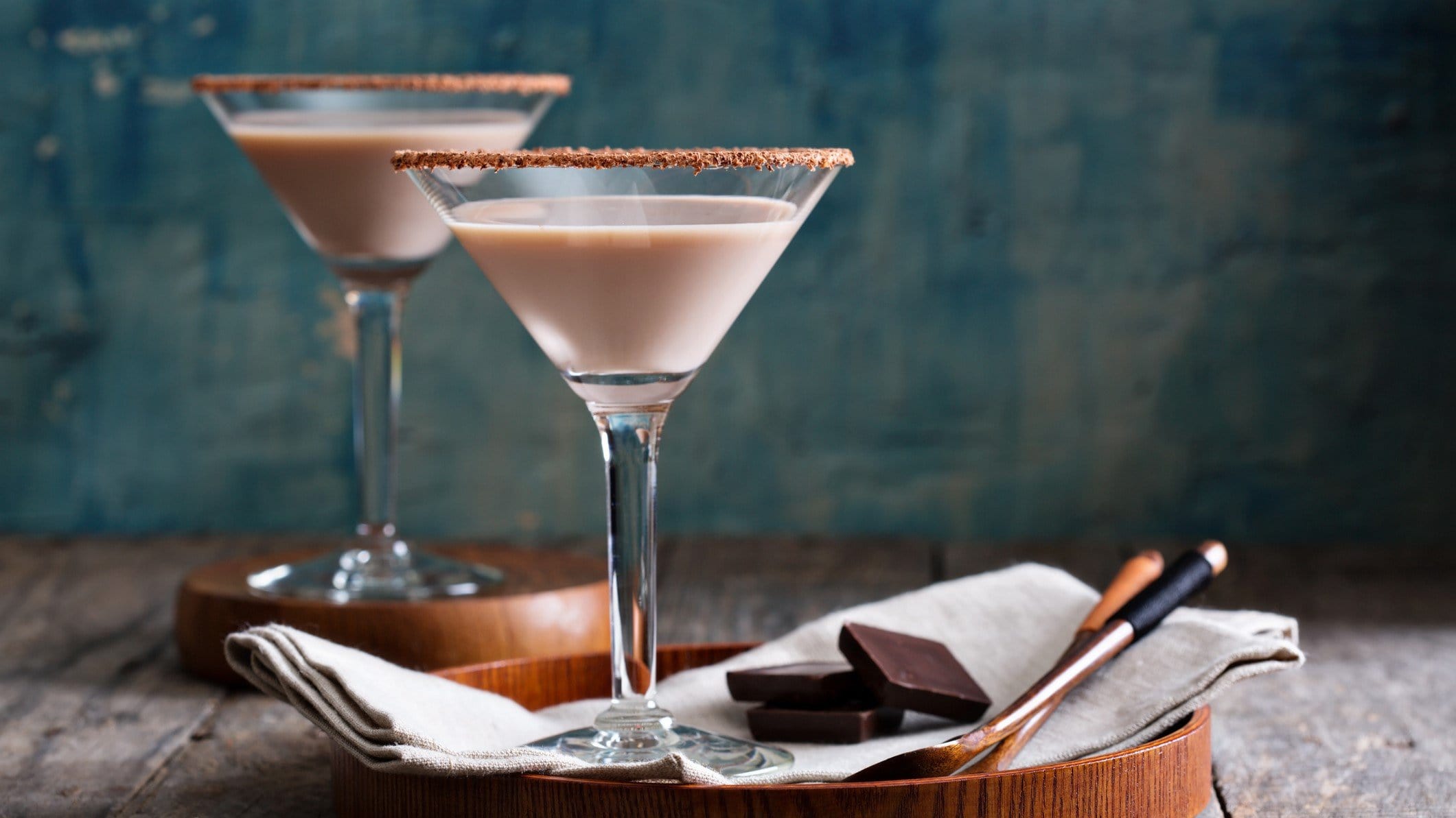 Zwei Nougatini mit dunkler Schokolade und Cocktailzubehör auf Tisch. Frontalansicht.