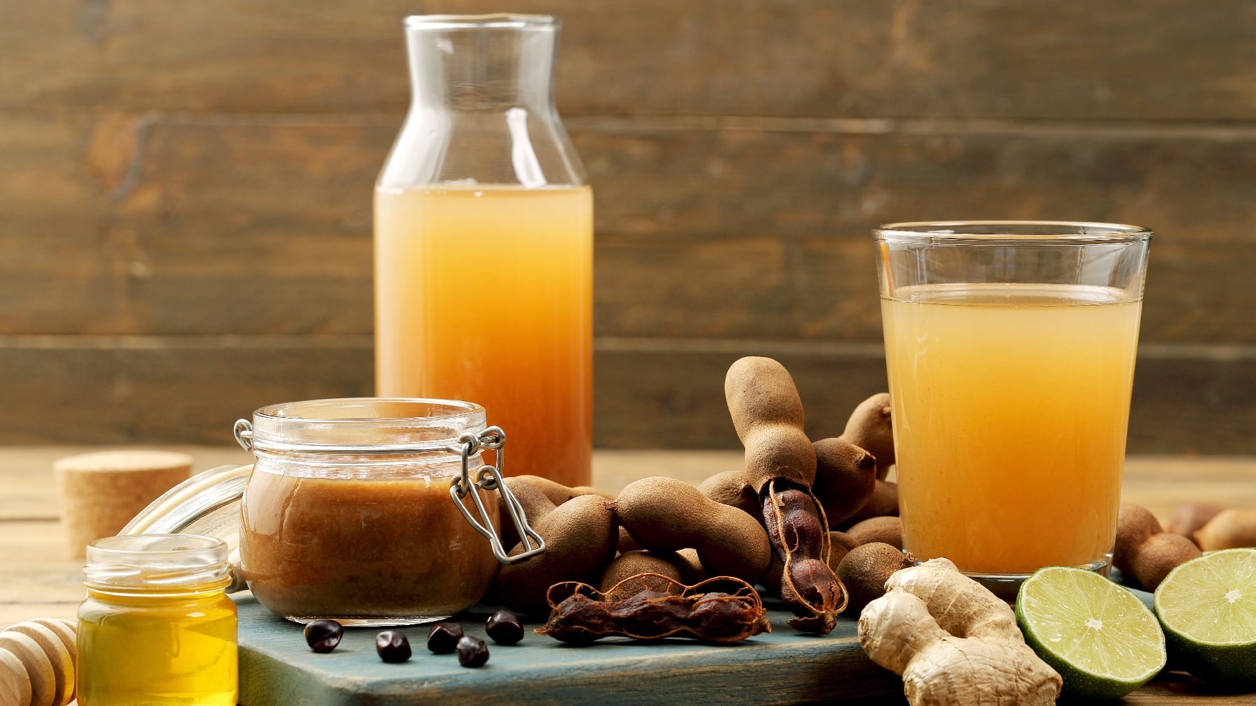 Ein Glas mit dem Tamarinden-Drink auf einem Holztisch mit Limette, Ingwer und Honig.