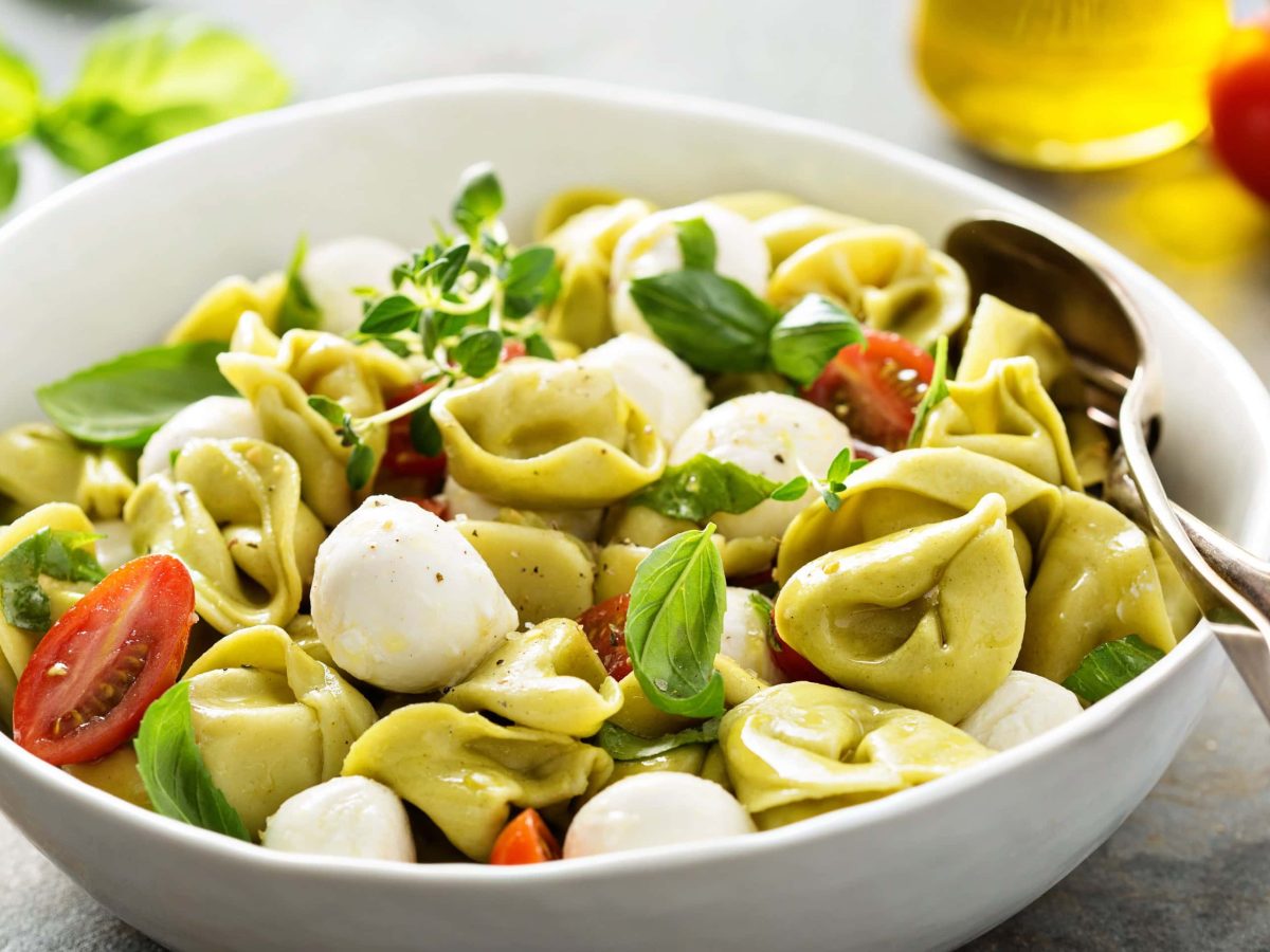 Schale mit Tortellini-Salat mitMOzzarella-Kügelchen, frischen Tomaten und Basilikum.