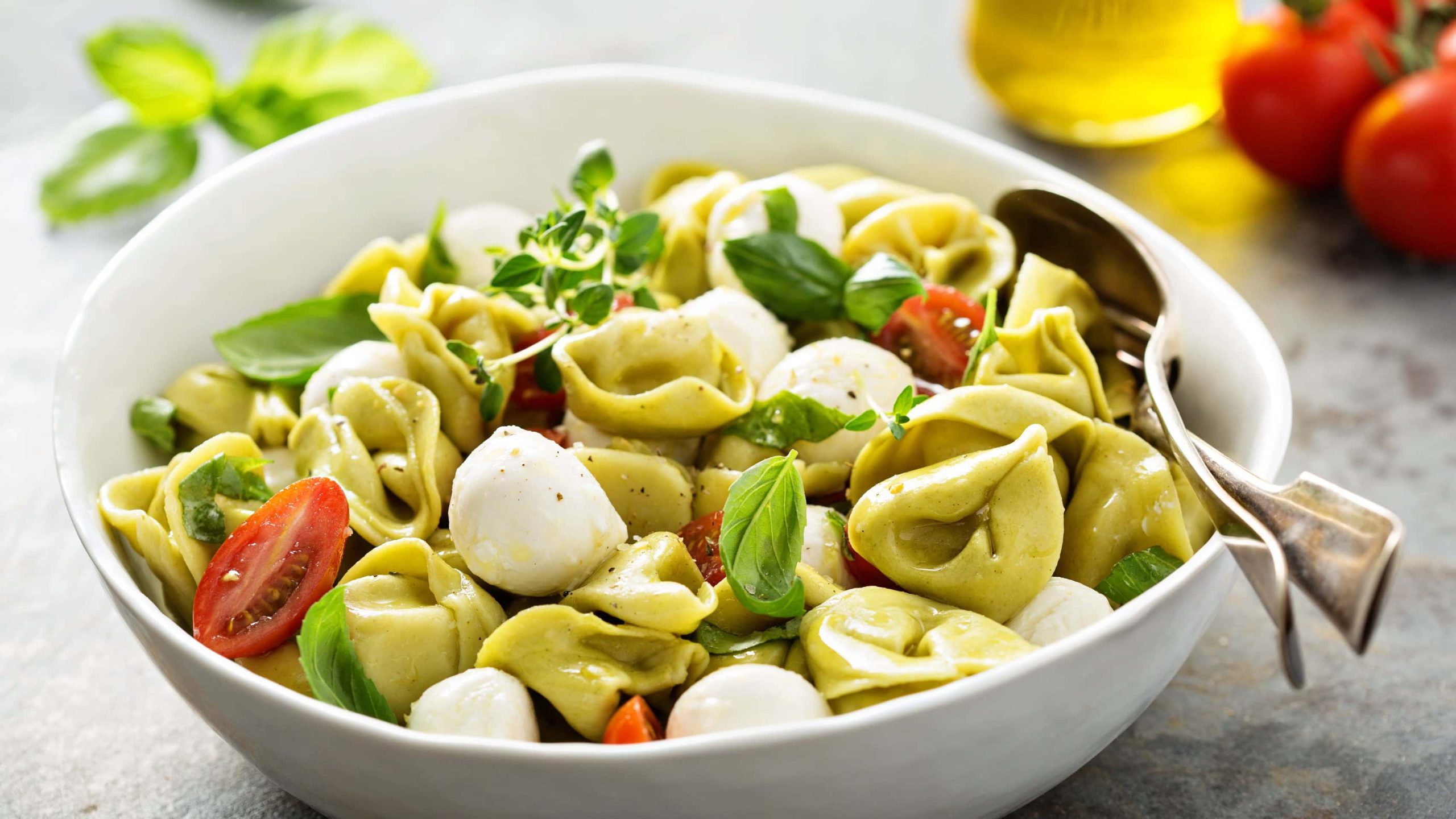 Schale mit Tortellini-Salat mitMOzzarella-Kügelchen, frischen Tomaten und Basilikum.
