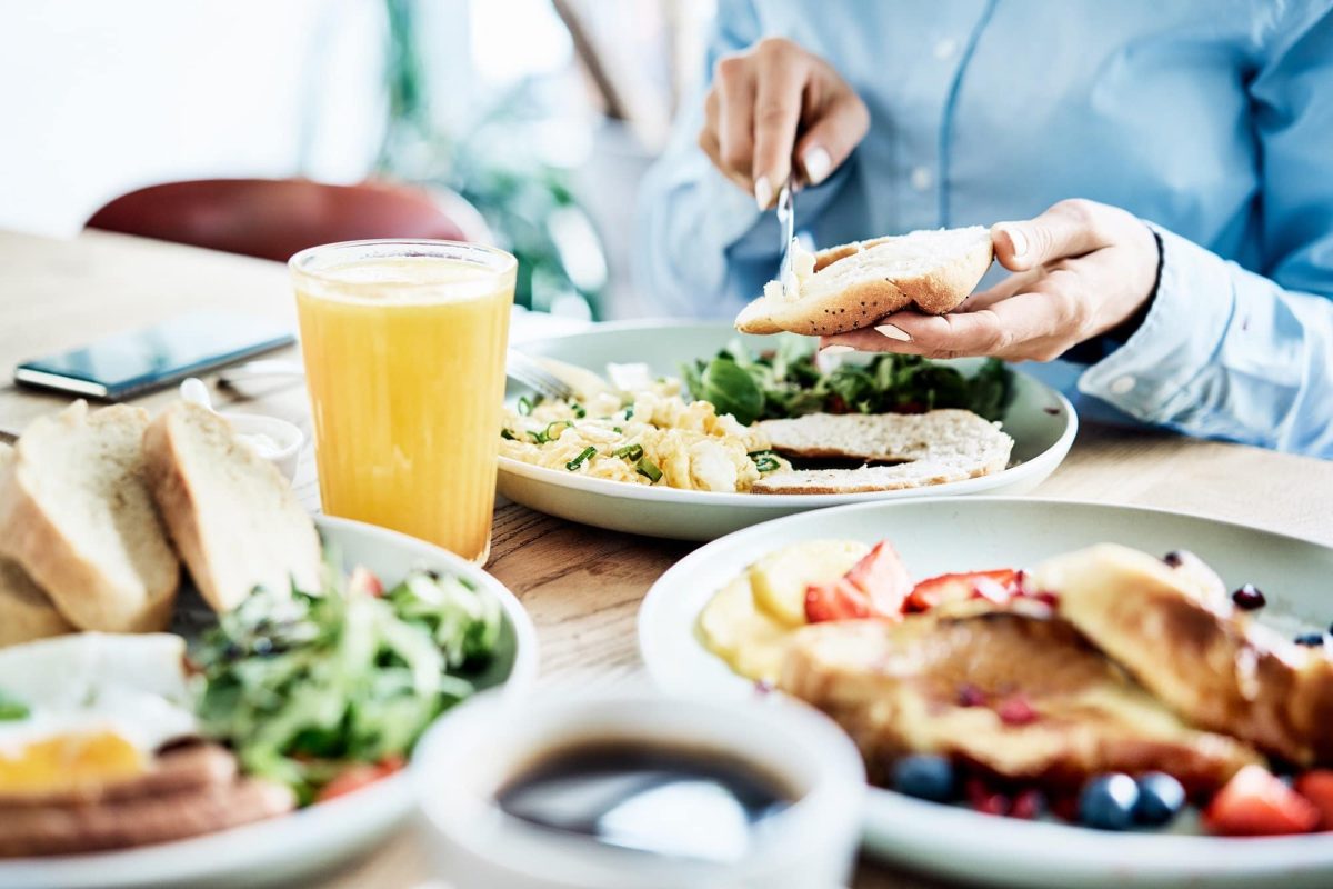 Die beliebtesten Brunch-Lokale Deutschlands: Eine Frau sitzt einem gedeckten Frühstückstisch, schmiert sich ein Brötchen, vor ihr volle Teller.
