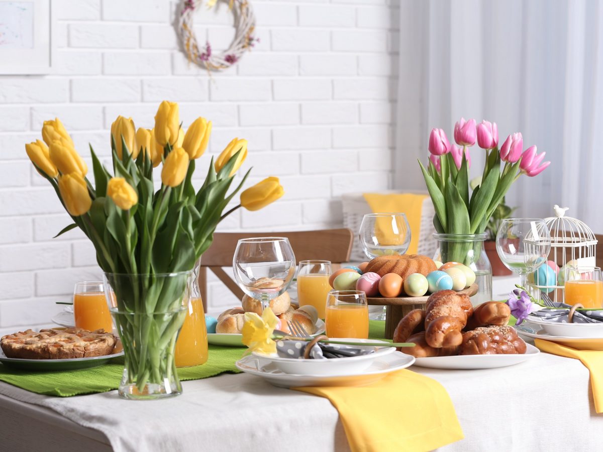 Tisch mit Tulpen, Ostergebäck, teller, Gläsern mit Orangensaft und anderer Deko.