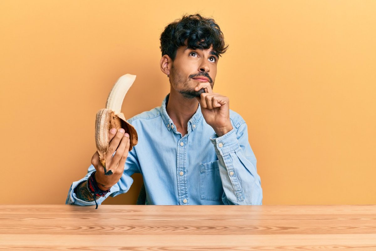 Sind Bananen vegan: Ein junger Mann mit nachdenklichem Blick hält eine geschälte Banane in der Hand.