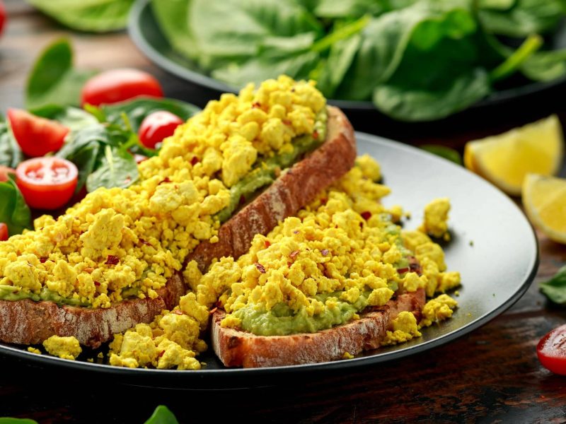 Test veganes Ei: Zwei Brotscheiben mit Guacamole und veganem Ei auf einem Teller, daneben angerichtet ein Salat.