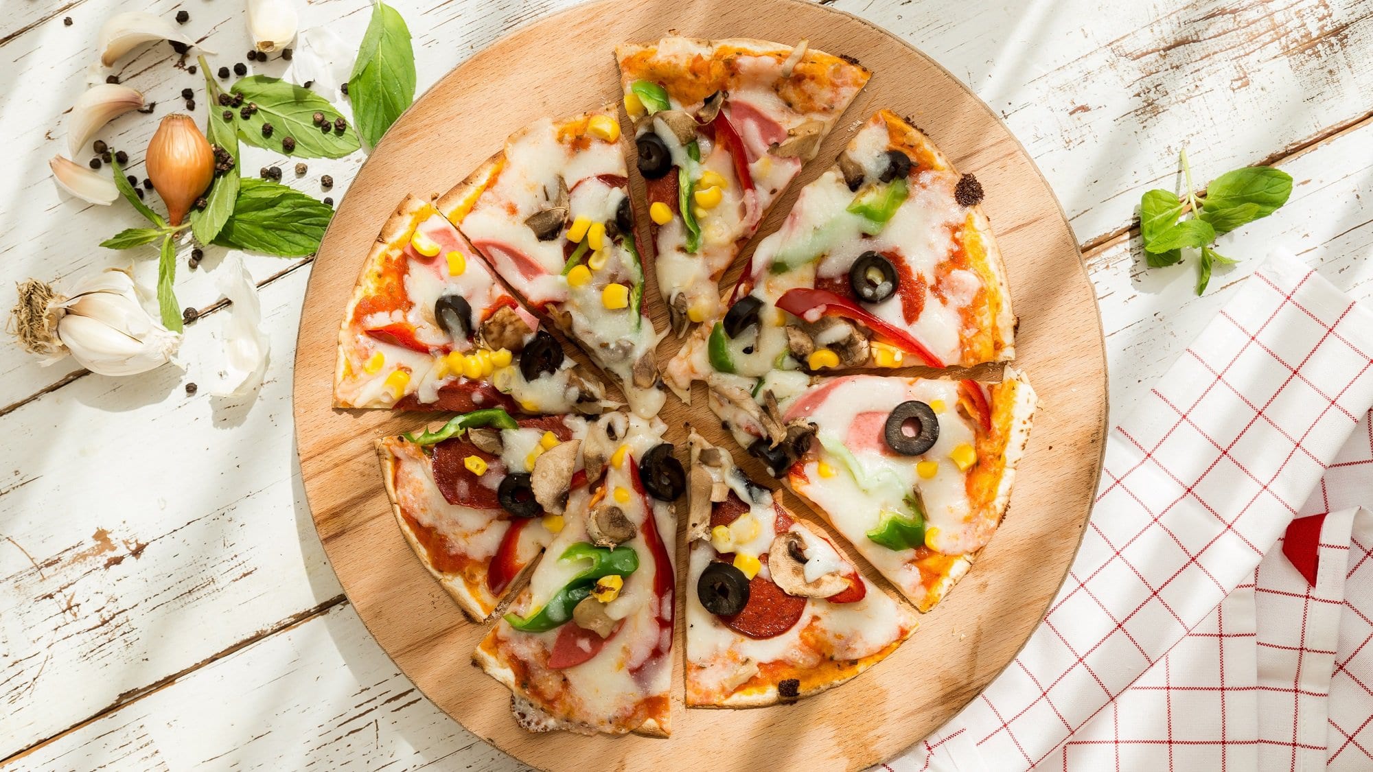 Eine geschnittene Tortilla-Pizza aus der Pfanne in der Draufsicht, belegt mit Oliven, Käse, Salami, Paprika und Mais.