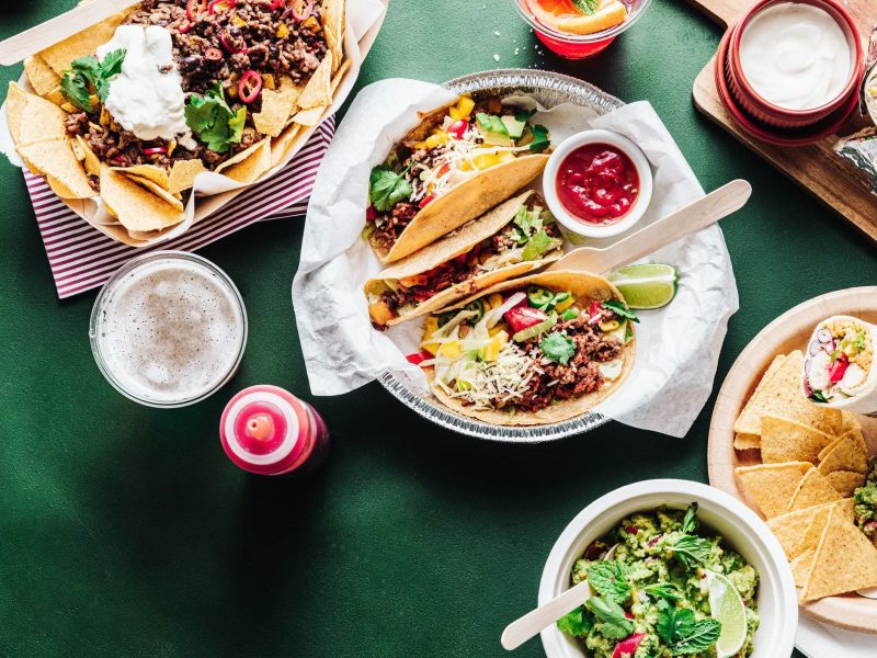 Zum Tag des Burrito der Unterschied zwischen Burritos und Wrap diverse Wraps und Tacos auf einem grünen Tisch mit Dips und Schalen. Draufsicht.