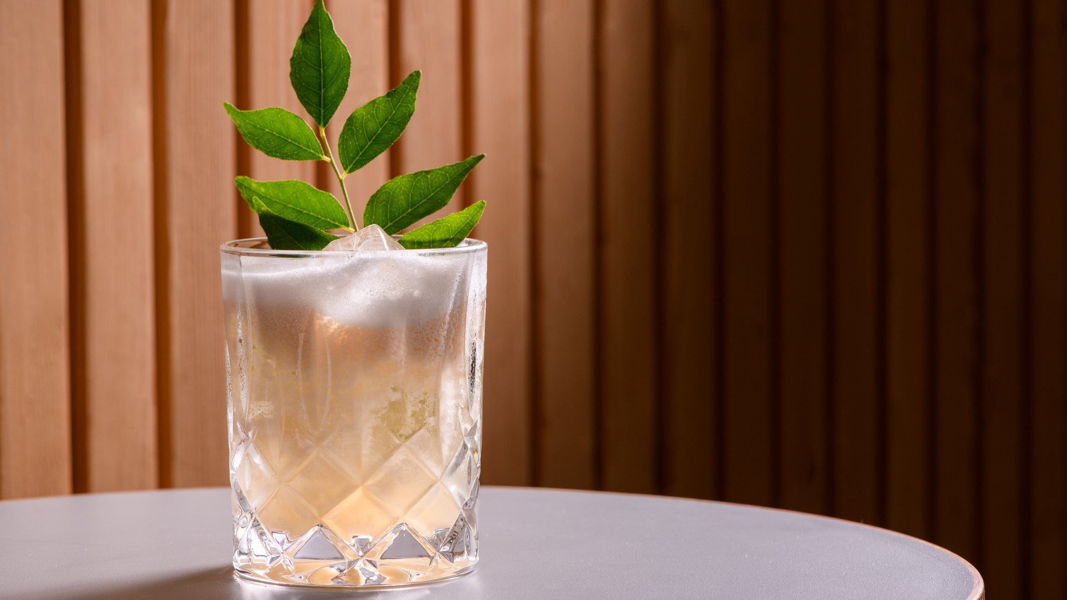 Lemon Vodka Rasam mit einem Zweig Curry-Blättern auf Tisch vor Holzhintergrund. Frontalansicht.