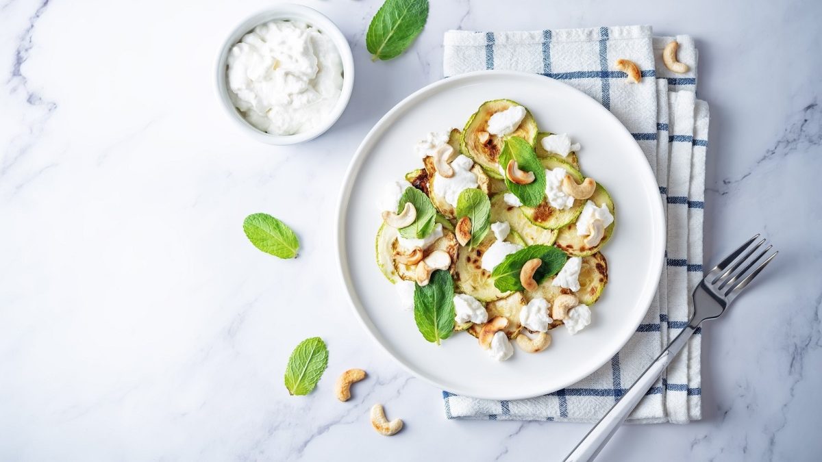 Ein weißer Teller mit Zucchini-Salat mit Ricotta auf einem Küchentuch.
