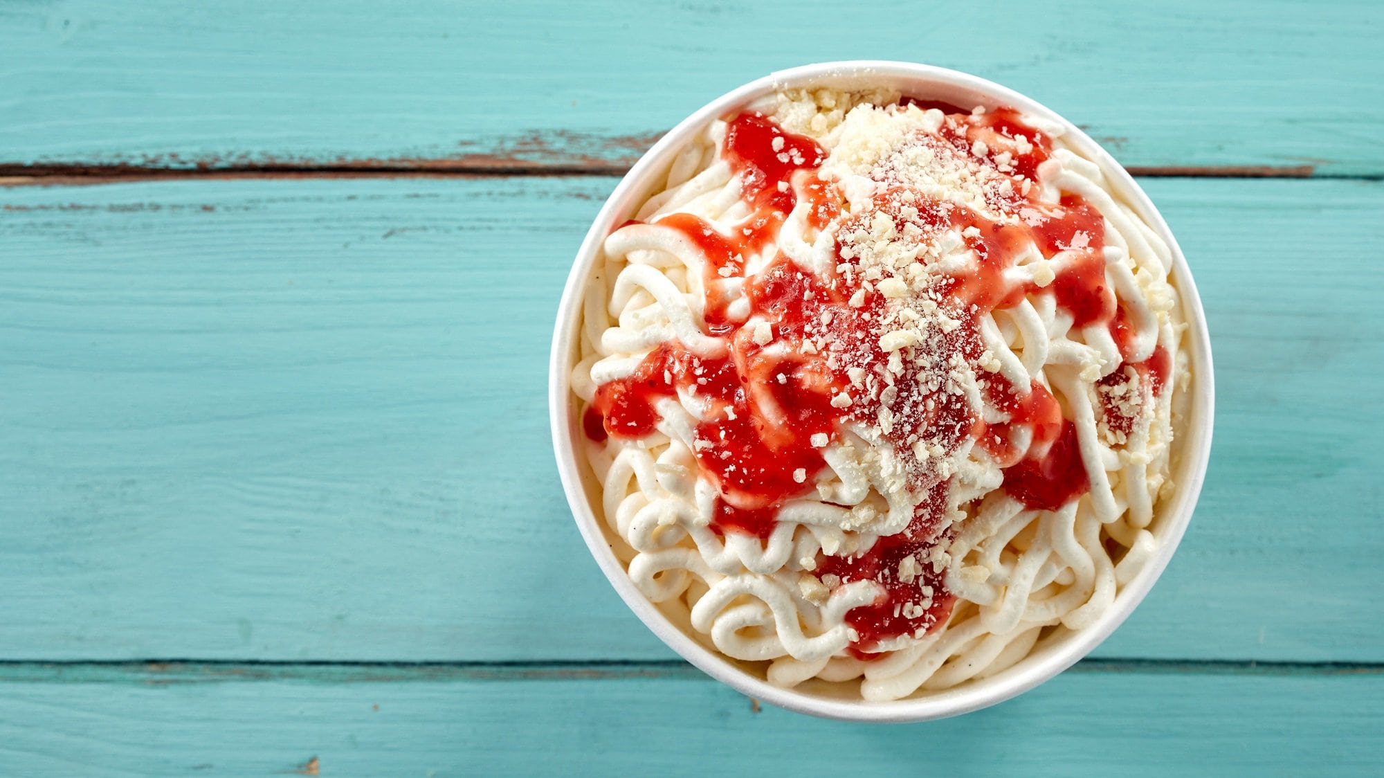 Ein Becher Spaghetti-Eis mit Erdbeersauce und Schokosplittern in der Draufsicht.