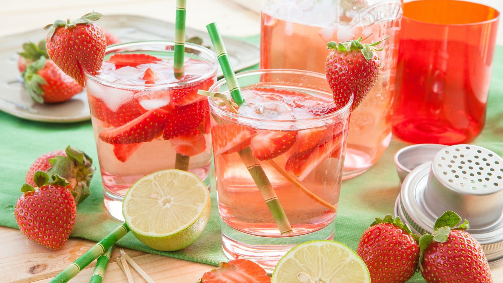 Zwei Gläser Alkoholfreie Erdbeerbowle mit frischen Erdbeeren und Eiswürfeln, drumherum Erdbeeren und Limetten.