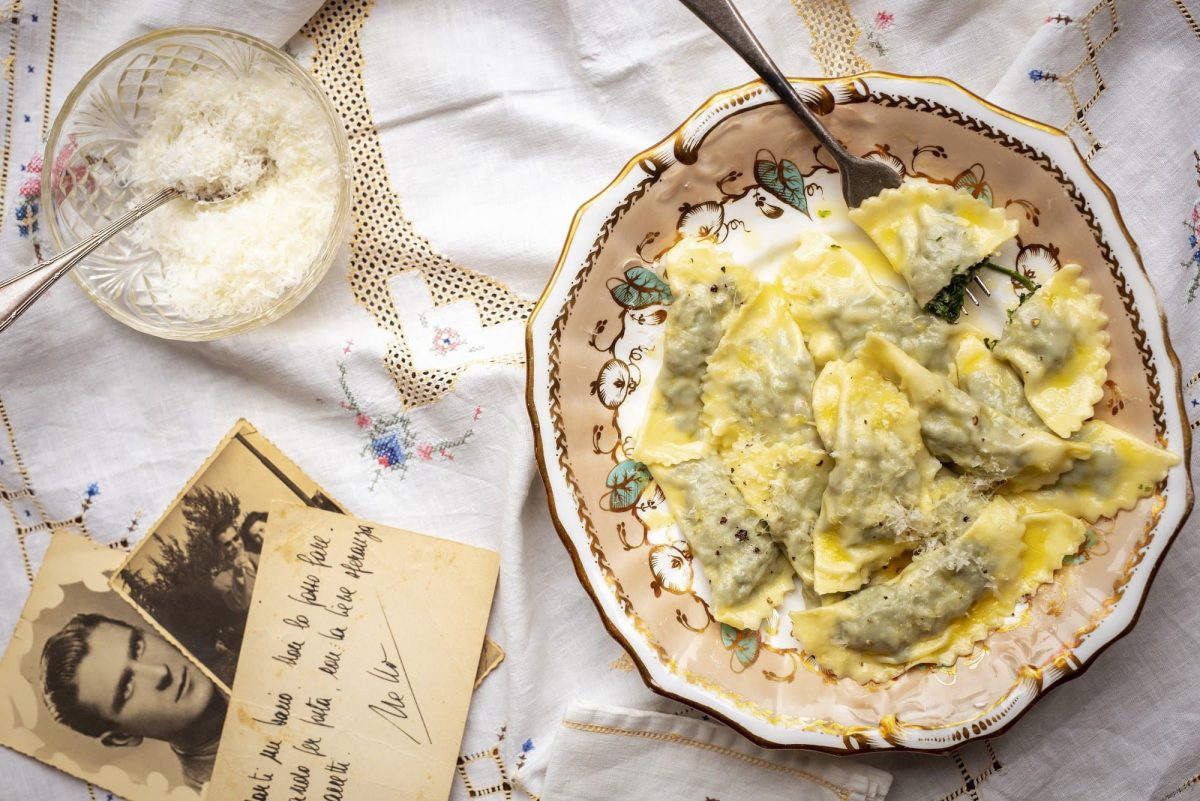 Istrien: Blattgemüse-Ravioli auf einem Teller in der Draufsicht, daneben alte Schwarz-Weiß-Fotos und eine Schale geriebener Käse.
