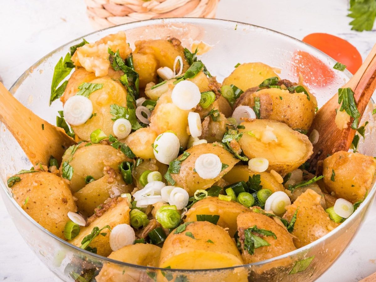 Eine Harissa-Kartoffelsalat mit Frühlingszwiebeln, darin auch Salatbesteck aus Holz.