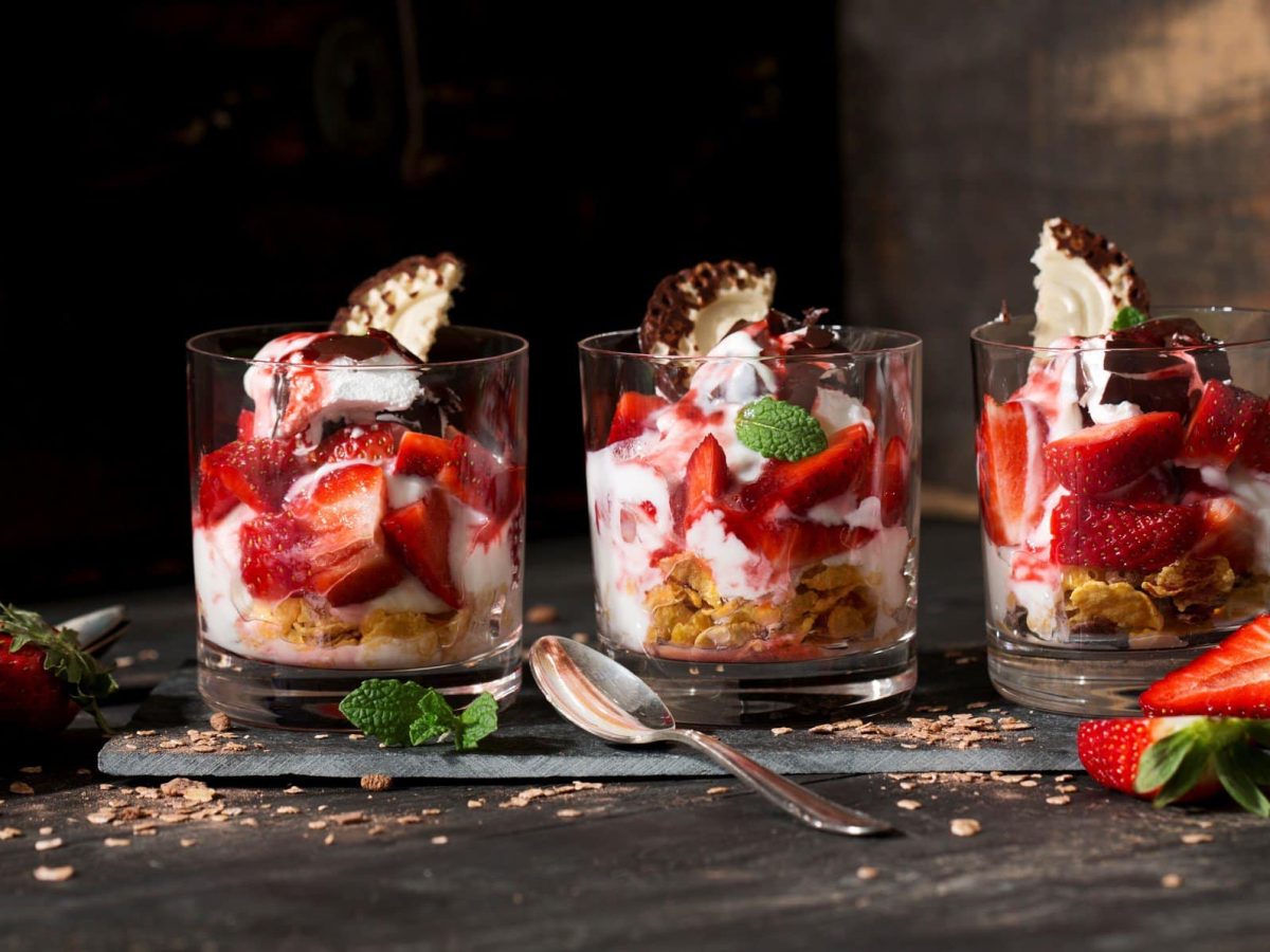 Schokokuss-Erdbeer-Dessert in drei durchsichtigen Gläsern vor rustikalem Ambiente.