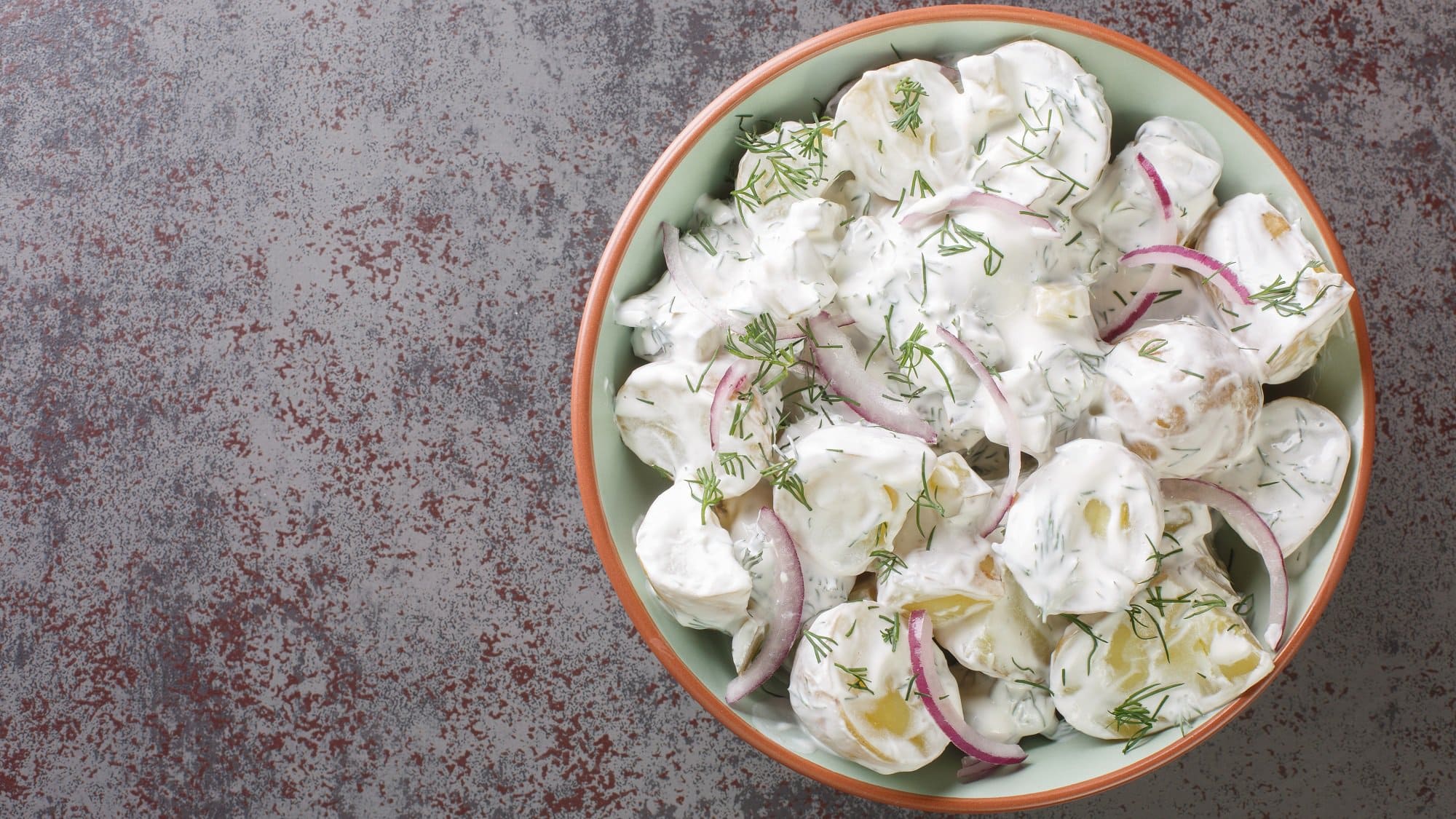 Eine Schüssel schwedischer Kartoffelsalat mit roten Zwiebeln, Dill und weißer Sauce.