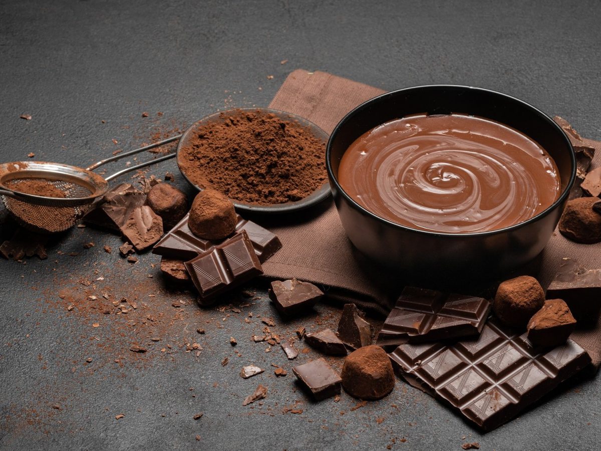 Eine Schüssel selbst gemachte Schokoladencreme, darum Schokoladentafeln, Kakaopulver und Kakaobohnen.