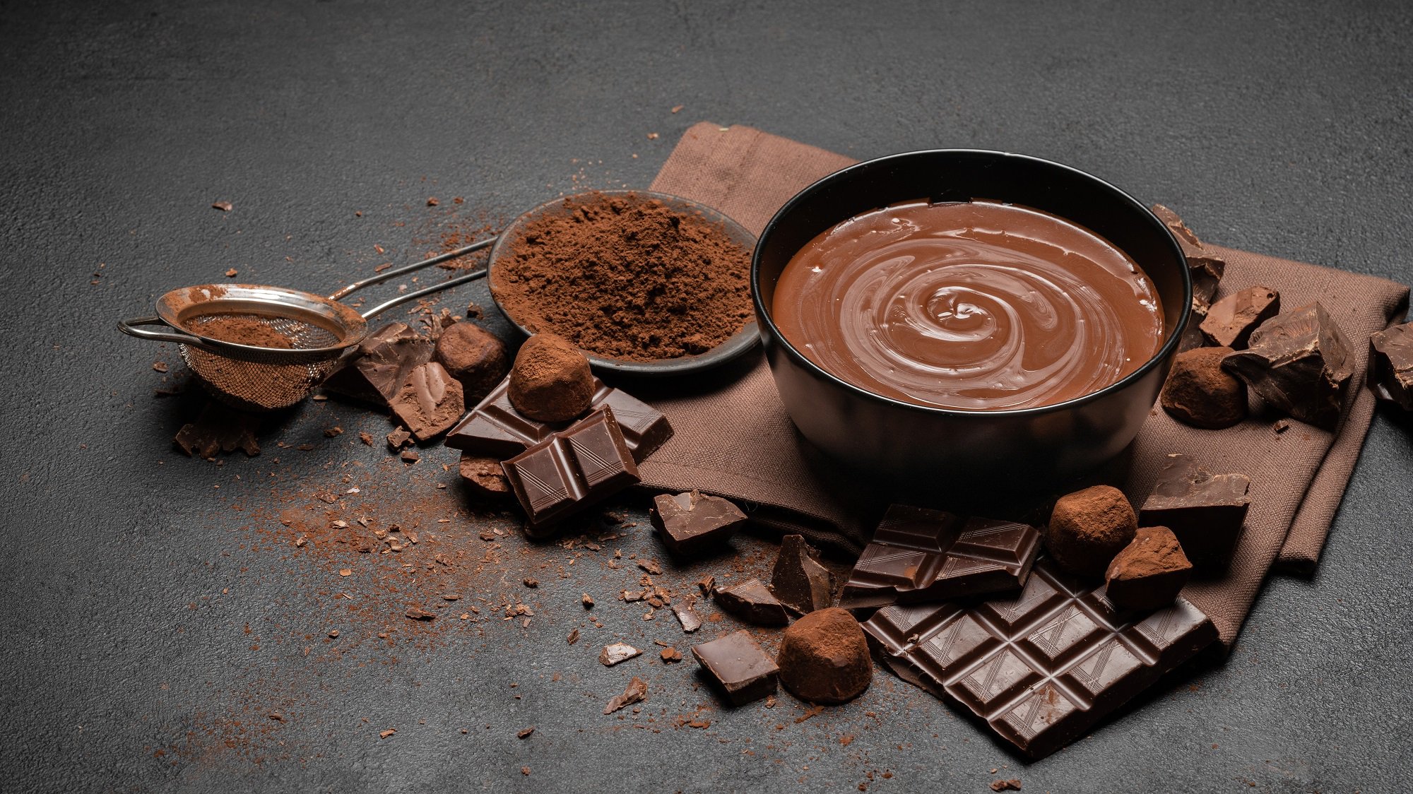 Eine Schüssel selbst gemachte Schokoladencreme, darum Schokoladentafeln, Kakaopulver und Kakaobohnen.
