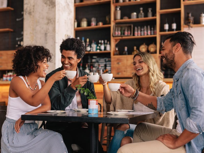 Vier Menschen an einem Tisch, die einen Slow Coffee trinken und dabei anstoßen.