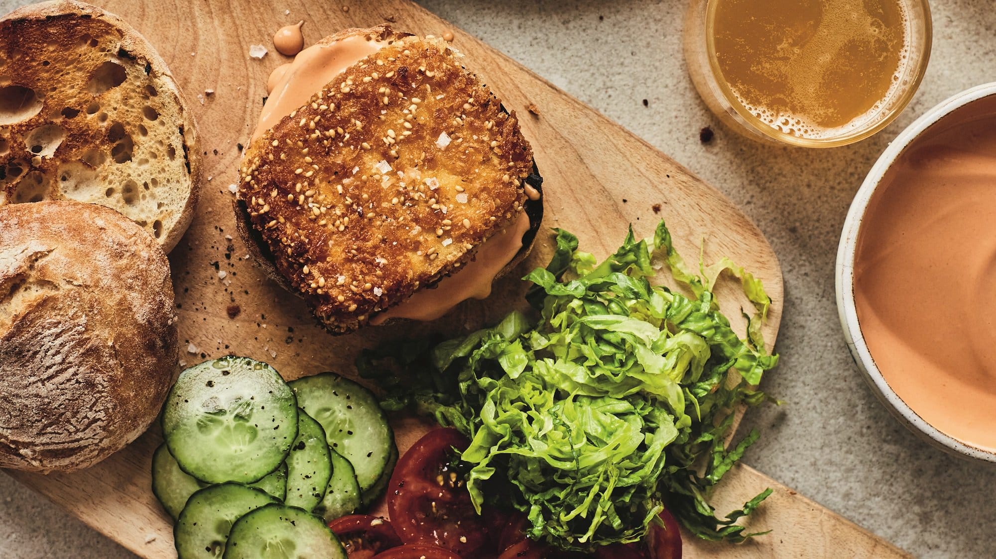 Tofu-Burger auf einem Brett, auf dem frische Tomaten, Gurken und Salat geschnitten liegen. Alles Draufsicht.