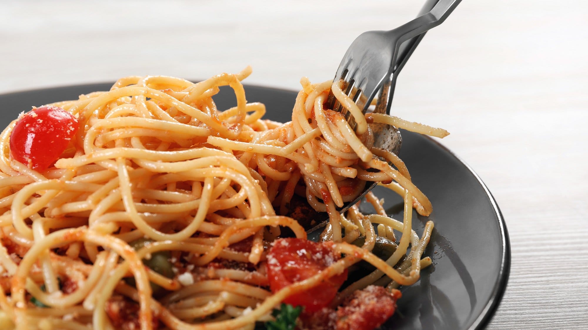 Ein Teller Tomaten-Creme-Pasta, eine Gabel und ein Löffel drehen gerade Spaghetti auf.