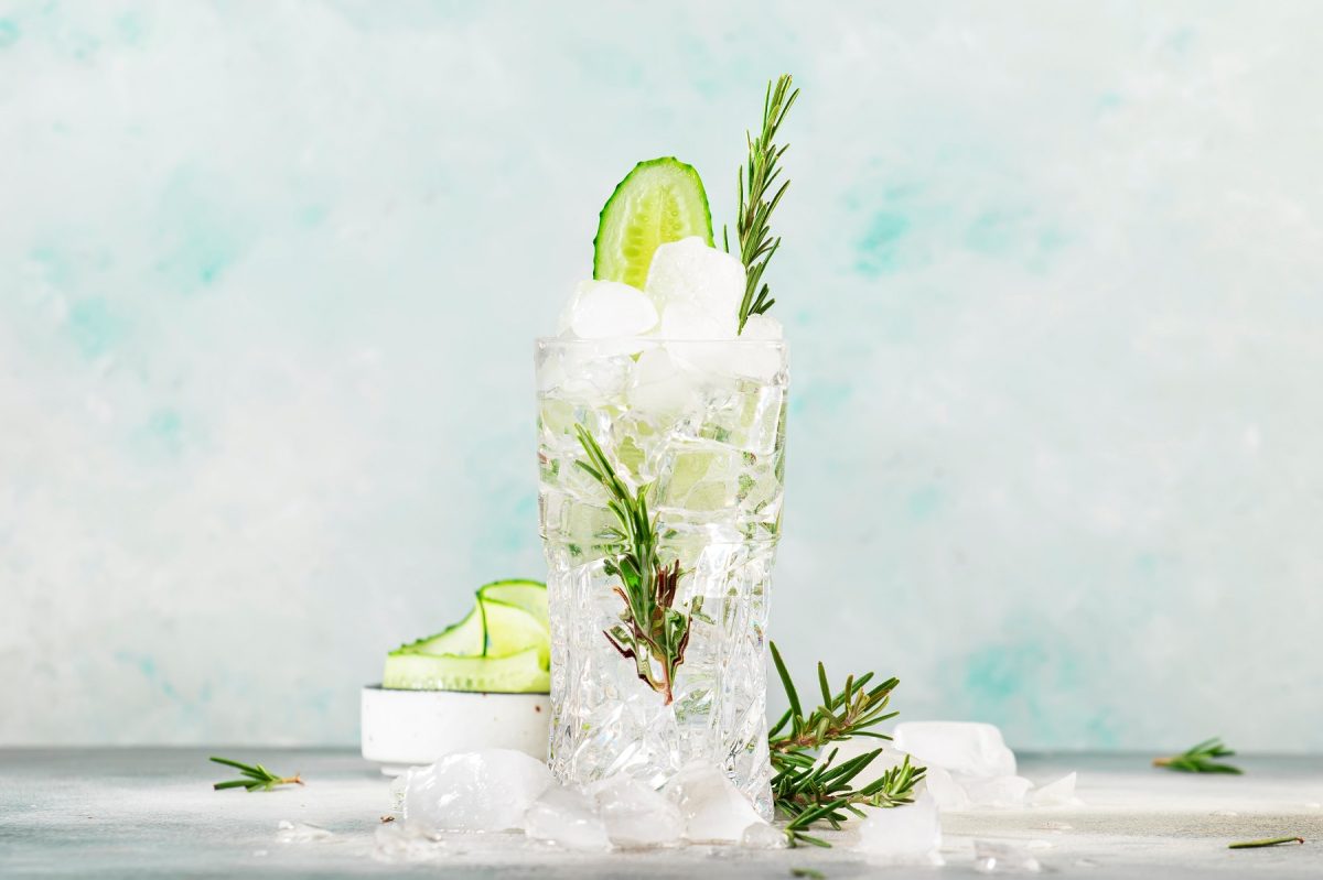 Erfrischender Gin Tonic mit Eiswürfeln, Gurkenscheibe und Rosmarinzweig in einem hohen Glas.