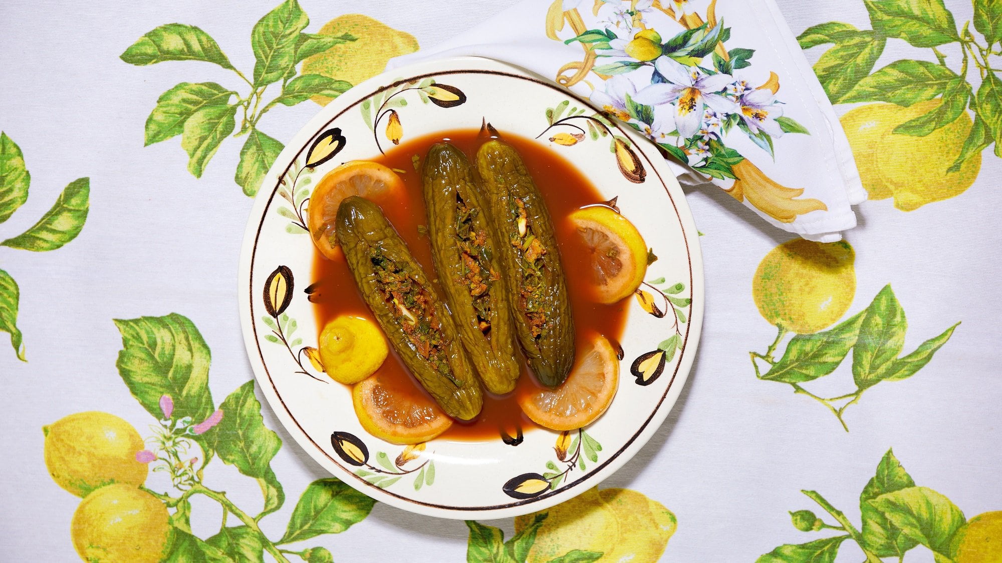 Drei gefüllte eingelegte Salatgurken, auch als Torshi Mahschie bekannt, auf einem Teller mit roter Sauce, Draufsicht.