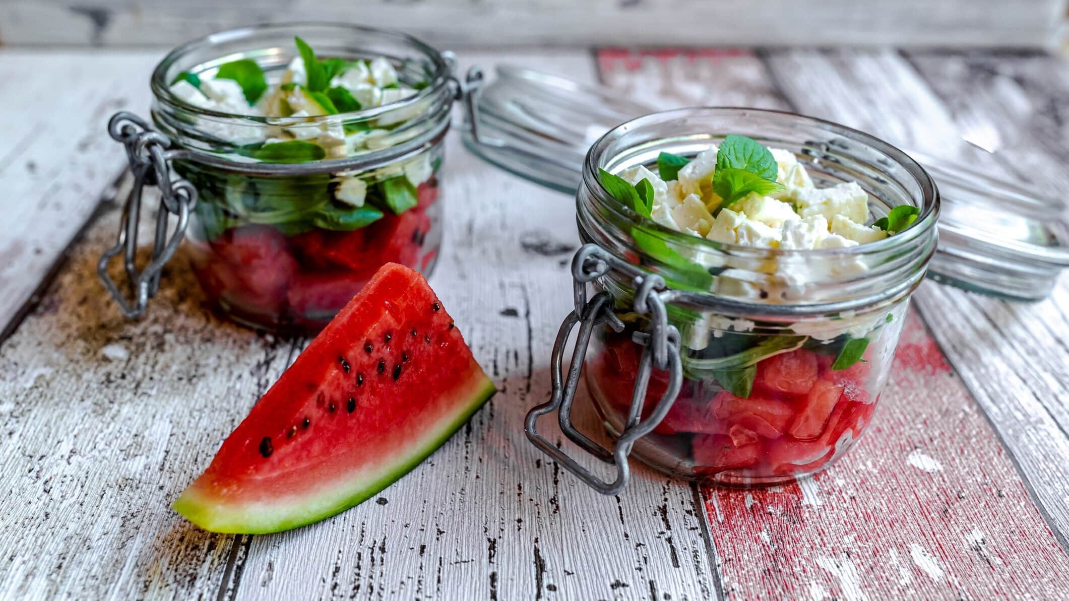 Frontal: Wassermelonensalat mit Feta und Minze im Glas, Schichtsalat auf hellem Holzboden.