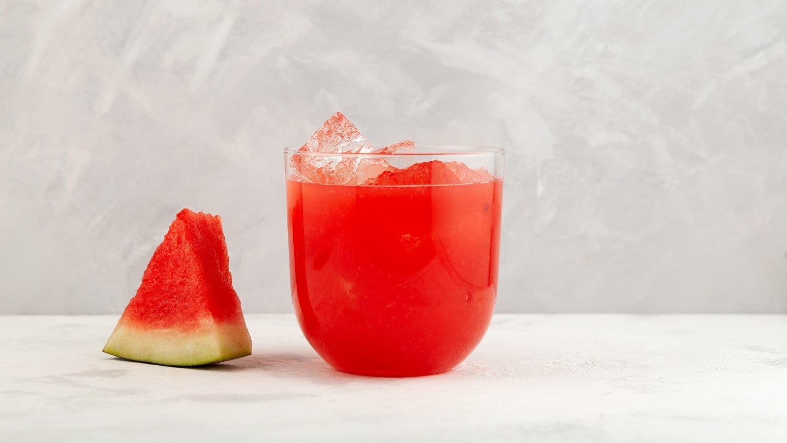 Ein Glas Agua fresca neben einem Stück Wassermelone.