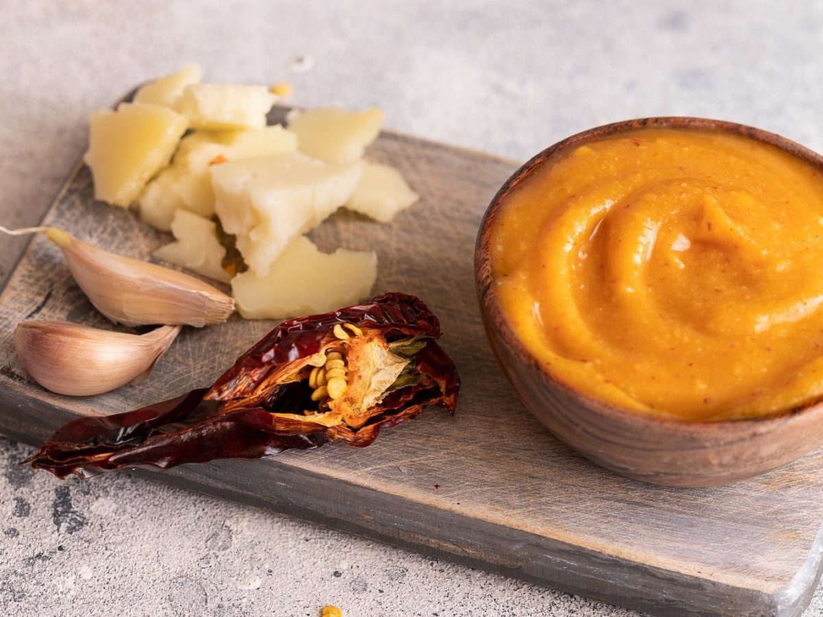 Eine kleine Holzschüssel mit Almogrote auf einem Schneidebrett mit Käse, getrockneter Paprika und Knoblauch.