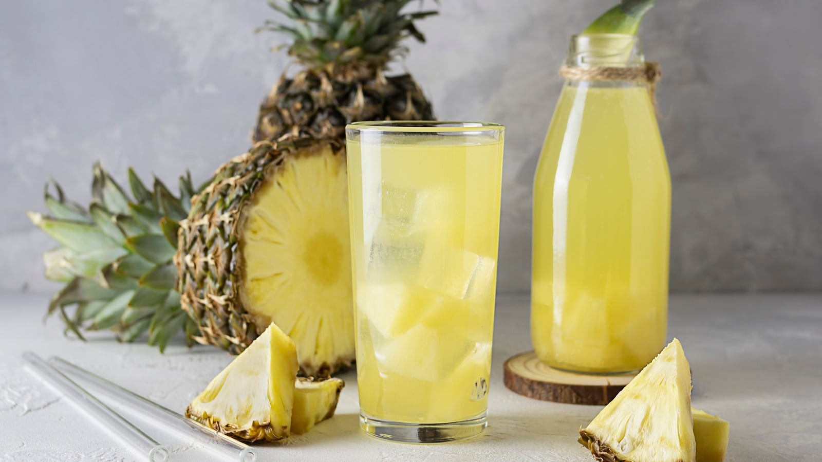 Ein Glas mit Ananas-Eistee vor einer frischen Ananas.