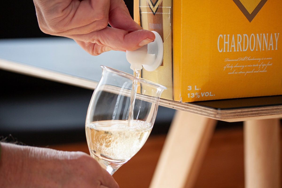 Frontal: ein Hand füllt einen Glas Wein aus einem Bag-in-Box-Wein-Karton ab.