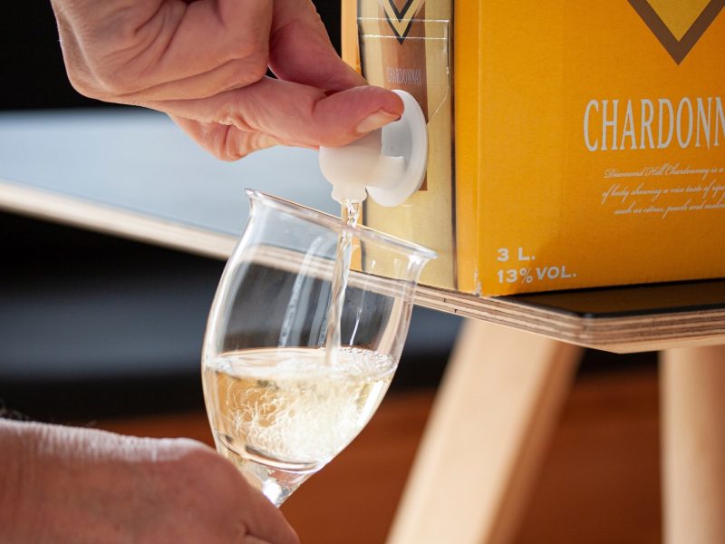Frontal: ein Hand füllt einen Glas Wein aus einem Bag-in-Box-Wein-Karton ab.