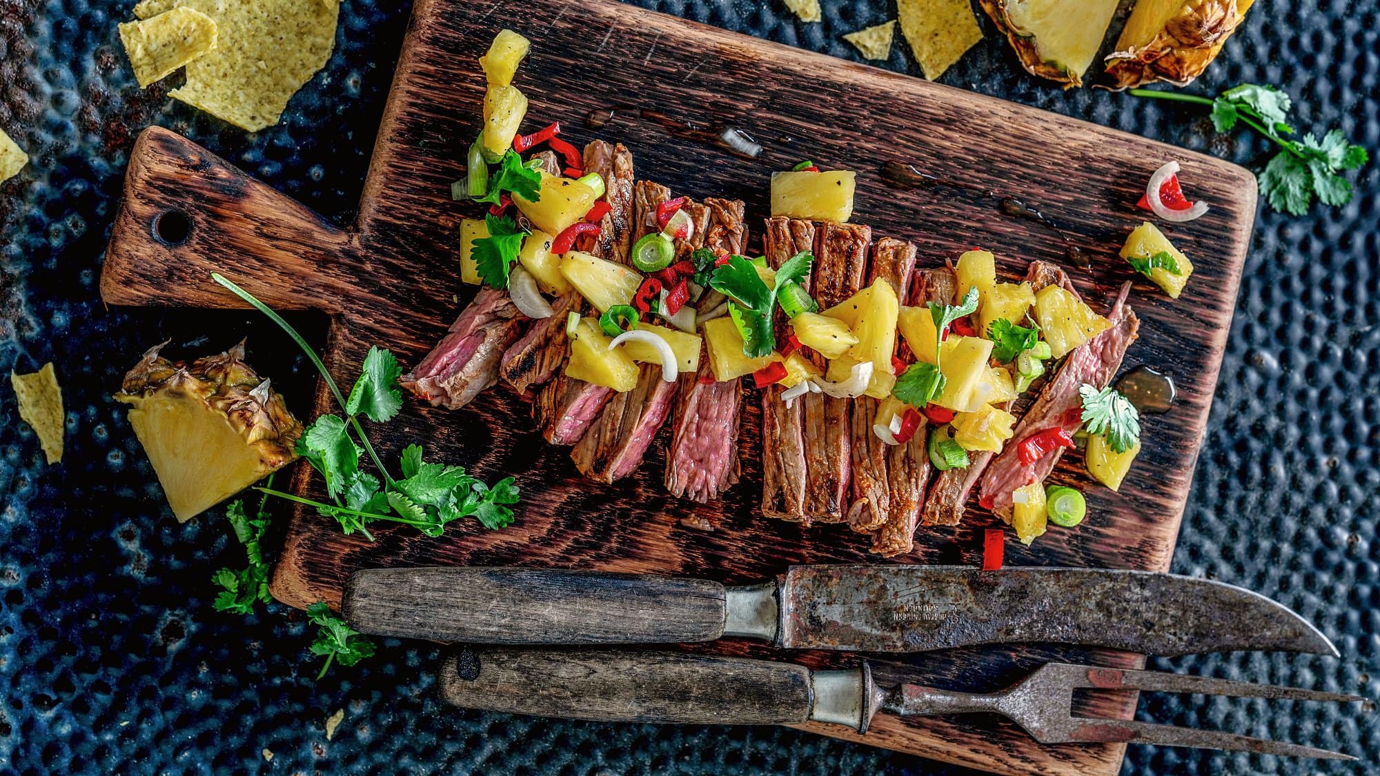 Carne Asada, gegrilltes Steak mit Ananas, in Scheiben geschnitten und auf einem Holzbrett angerichtet, daneben Nacho-Chips.