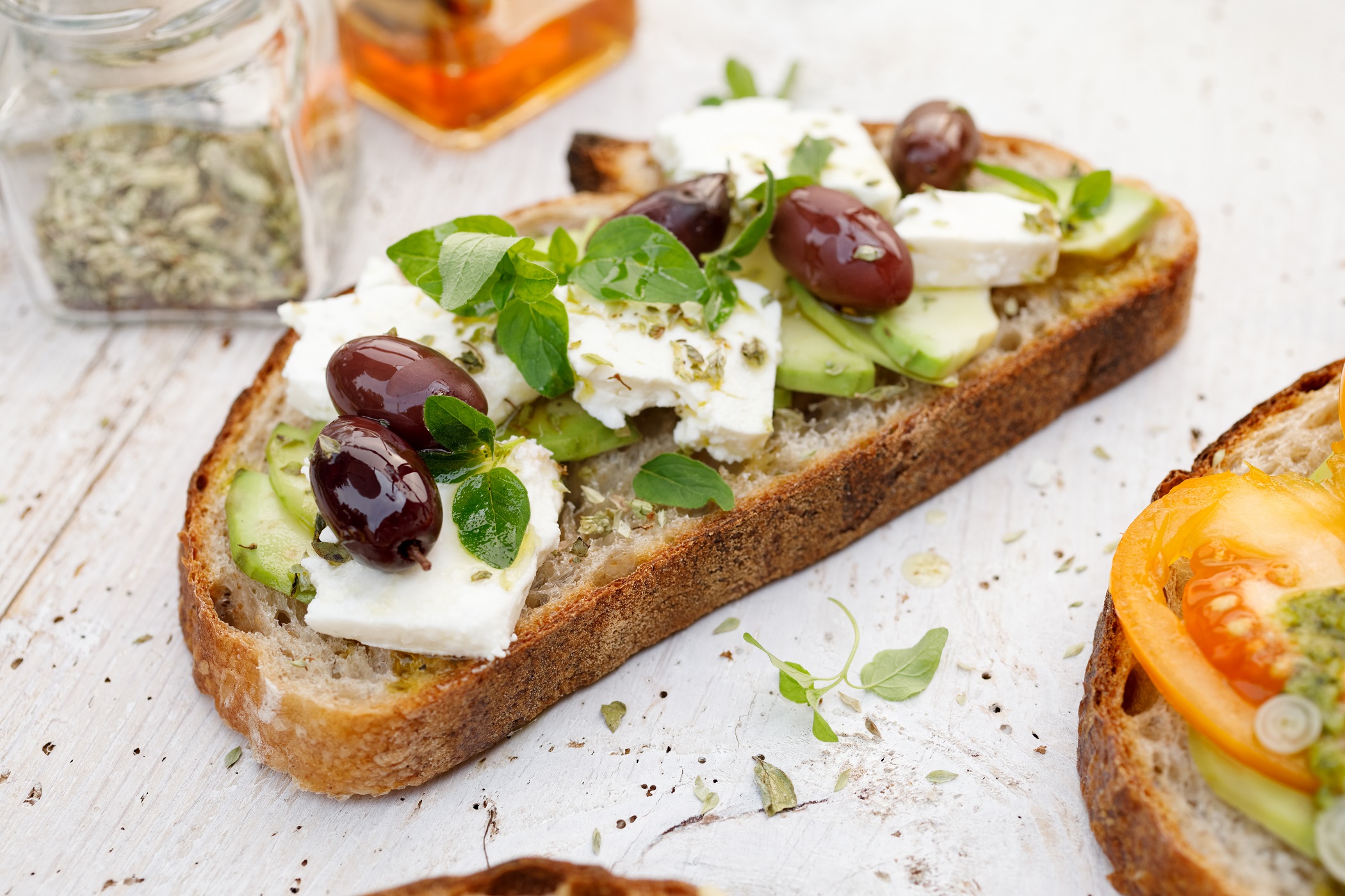 Draufsicht: Ein griechisches Sandwich mit Oliven und Feta und Oregano liegt auf einem weißen Holztisch.