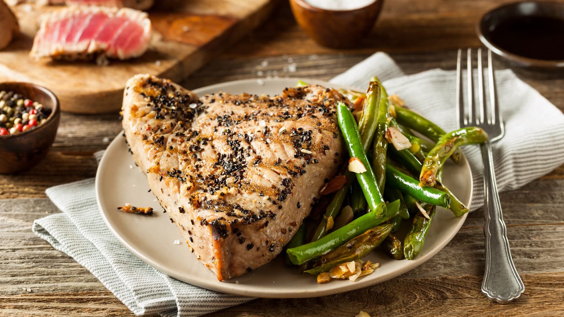 Ein weißer Teller mit dem Thunfisch-Steak auf einem Holztisch mit Gewürzen.