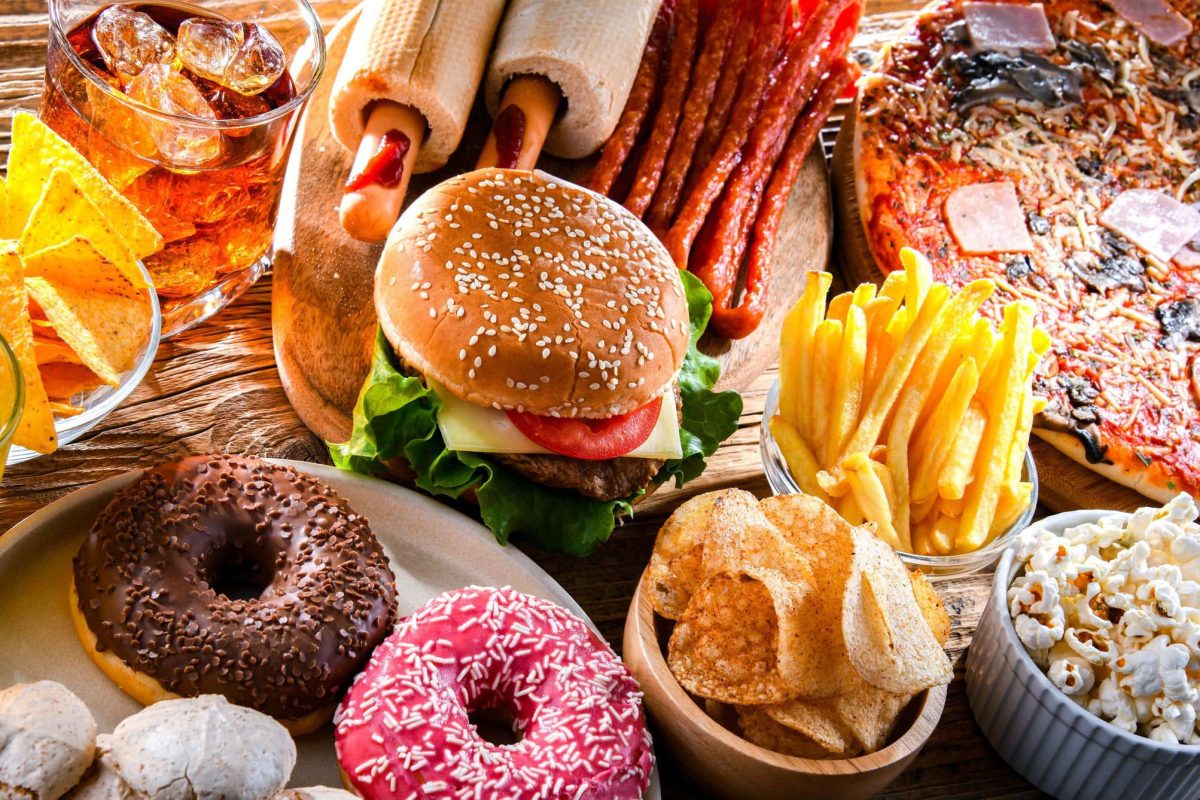 Was ist der Unterschied zwischen Fast Food und Junkfood? Diverses Junkfood nebeneinander im Bild verteilt. Was gehört alles zu Junkfood? Unter anderem Donuts, Pizza, Chips, Burger und Pommes. Draufsicht.