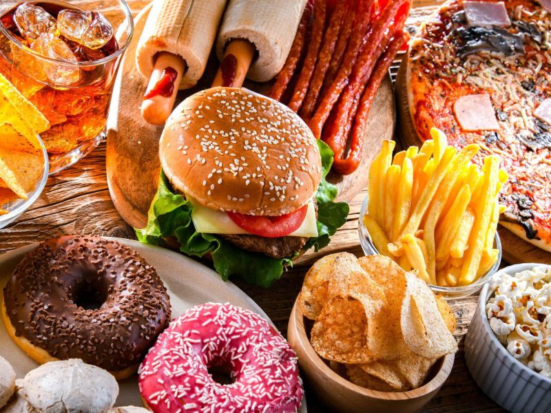 Was ist der Unterschied zwischen Fast Food und Junkfood? Diverses Junkfood nebeneinander im Bild verteilt. Was gehört alles zu Junkfood? Unter anderem Donuts, Pizza, Chips, Burger und Pommes. Draufsicht.