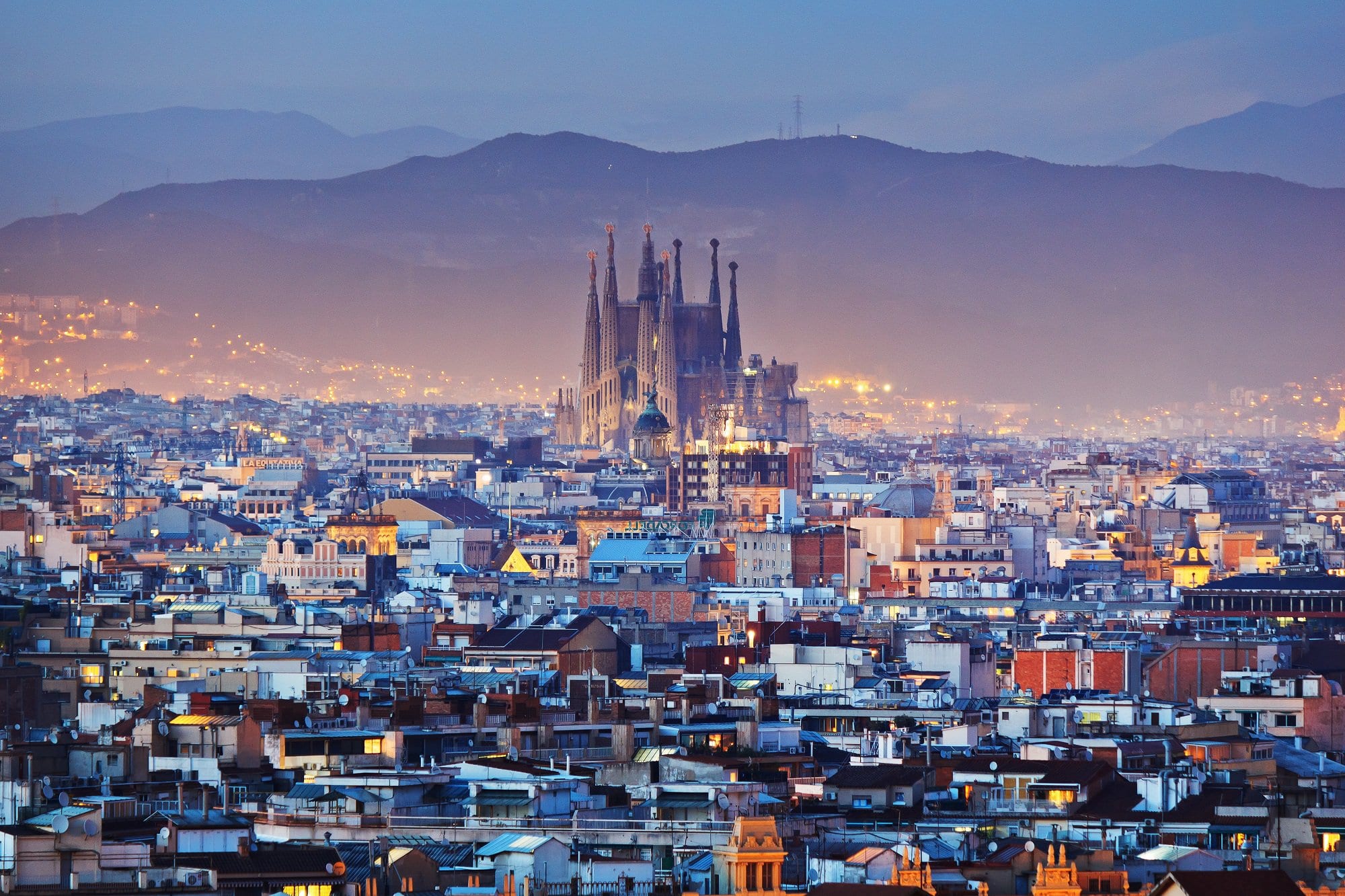 Vegane Städte: Blick auf Barcelonas Skyline mit der Sagrada und umliegender Häuser im Abendlicht, Berge im Hintergrund.