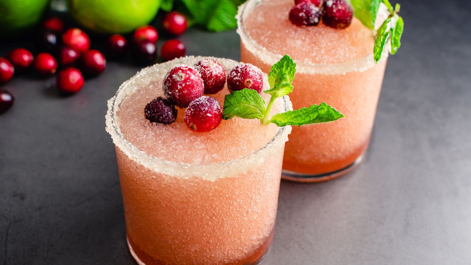 Draufsicht: zwei Frozen Cranberry Margarita. Im Bild Cranberrys, Minze und Limetten.