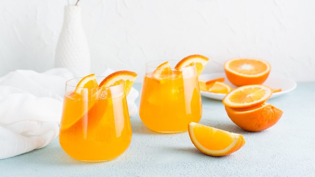 Zwei Gläser mit Orange Gin Fizz auf einem hellblauen Untergrund.