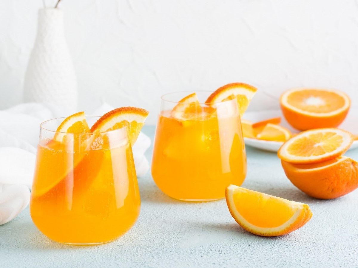 Zwei Gläser mit Orange Gin Fizz auf einem hellblauen Untergrund.