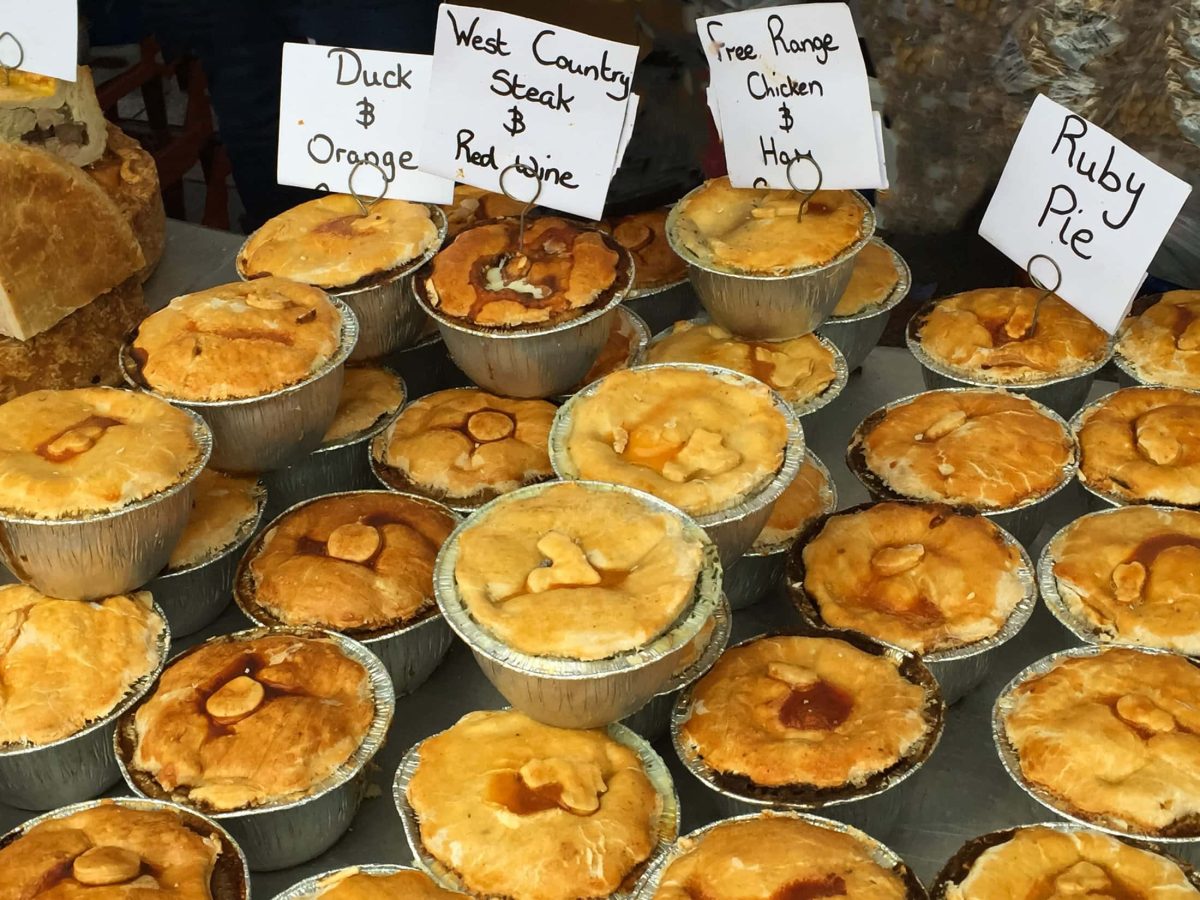 In einem Schaufenster sind viele verschiedene britische Pie-Varianten in kleinen Formen. Die Pies haben Schilder, auf denen die Pie-Rezepte und Pie-Namen stehen.