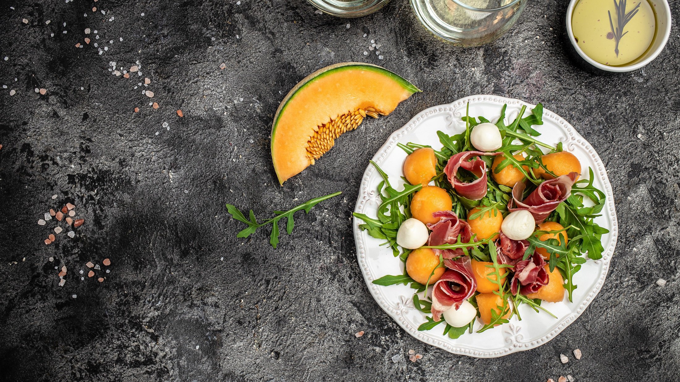 Draufsicht: Ein heller Teller süßer und fruchtiger Sommersalat mit Cantaloupe-Melone auf dunklem Untergrund.