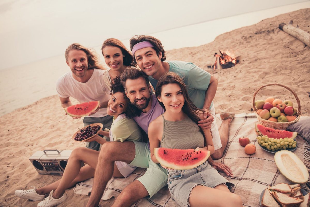 Strand, Hintergrund Meer. Eine Gruppe fröhlicher jungen Menschen mit Wassermelonen in den Händen schauen frontal in die Kamera.