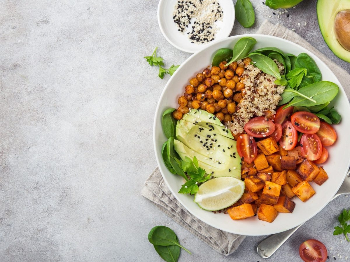 Eine Kürbis-Quinoa-Bowl in der Draufsicht mit Babysoinat, Kichererbsen und Avocado sowie einer Spalte Limette, drumherum frische Zutaten.