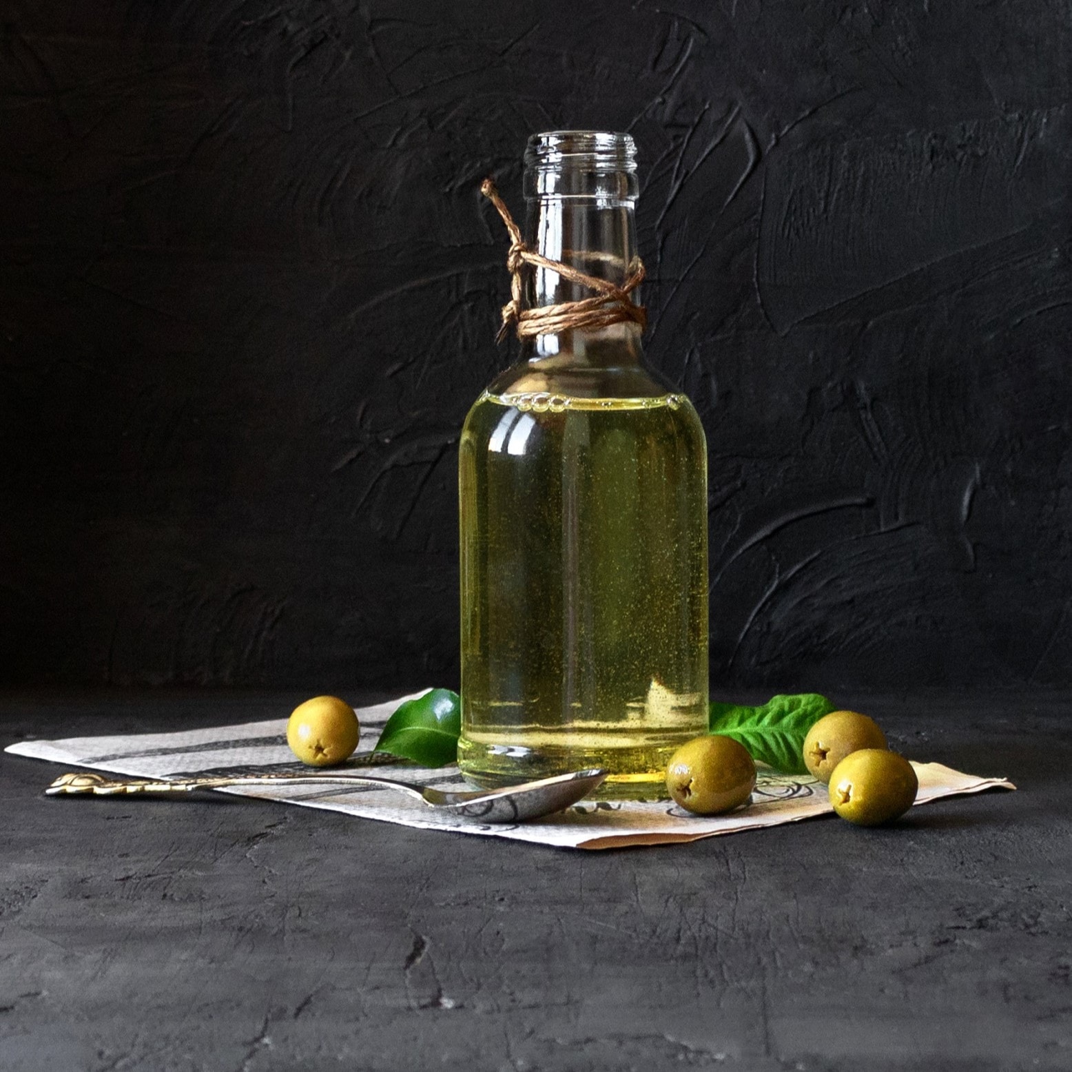 Olivenöl und grüne Oliven vor dunklem Hintergrund.